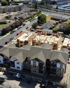 Aerial view of a residential construction site showing a multi-family housing complex in various stages of development, surrounded by completed homes and neighborhood infrastructure.