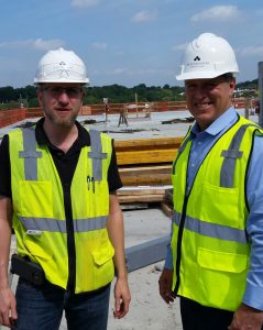 Two Hillmann Consulting construction professionals wearing hard hats and high-visibility vests standing on an active job site, highlighting project oversight and on-site collaboration during the building process.