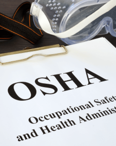 OSHA document on a clipboard labeled "Occupational Safety and Health Administration," with a pair of safety goggles and protective gear strap placed nearby, symbolizing workplace safety compliance.