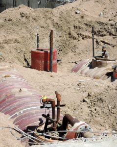 Large underground storage tanks partially exposed at a construction or excavation site. The cylindrical tanks are surrounded by dirt, with visible piping and fittings protruding from the top, indicating an environmental or fuel system installation or removal.