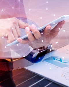 Close-up of hands using a digital tablet over technical documents with a network overlay effect, symbolizing the integration of technology, data, and smart planning in energy engineering or construction projects.
